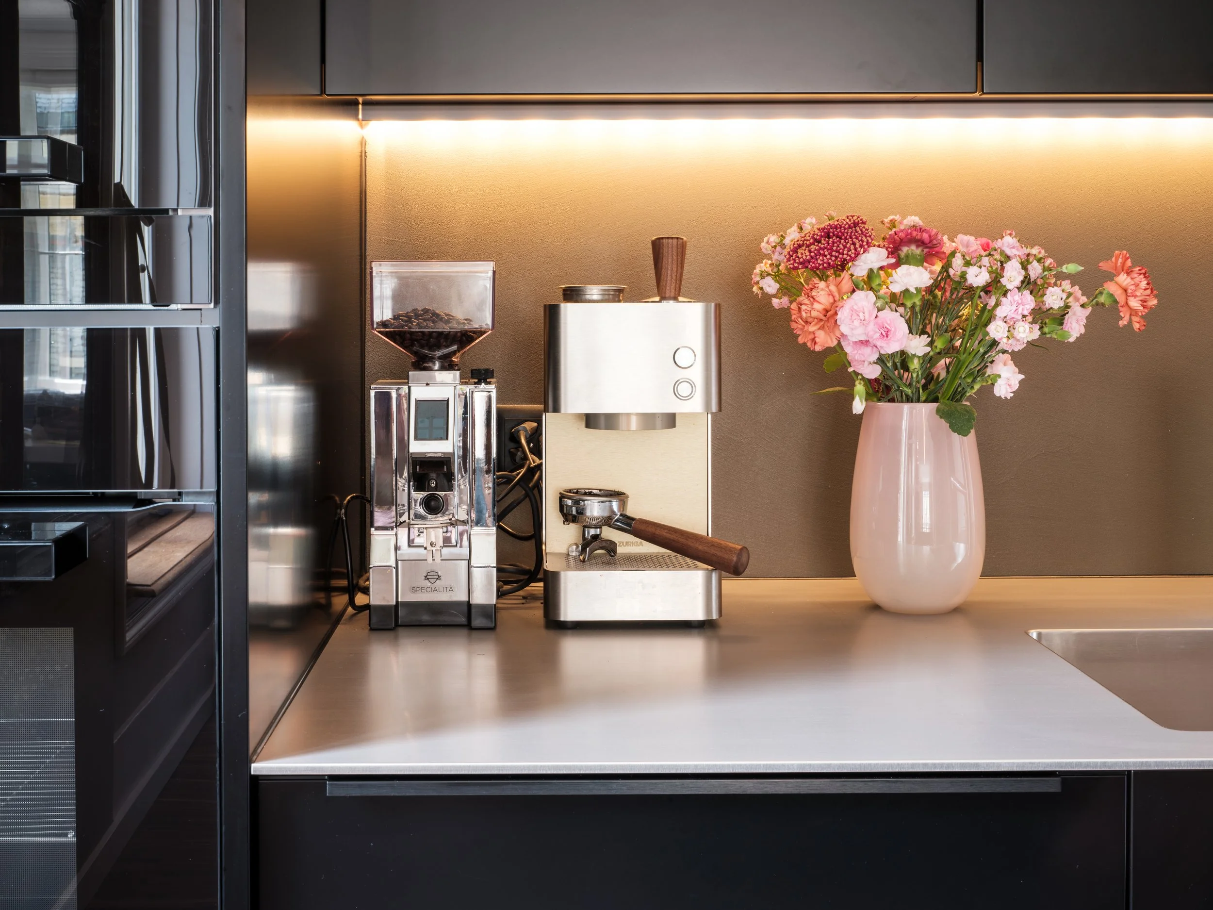 Küchenarbeitsplatte mit Kaffeemaschine und Blumenstrauß in einer Vase.