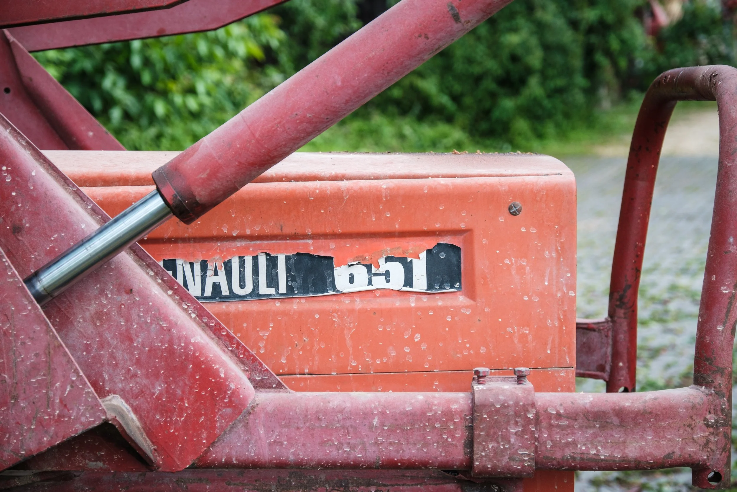 Ein alter, roter Traktor mit sichtbarer Hydraulikstange und einem abgenutzten schwarzen und weißen Aufkleber