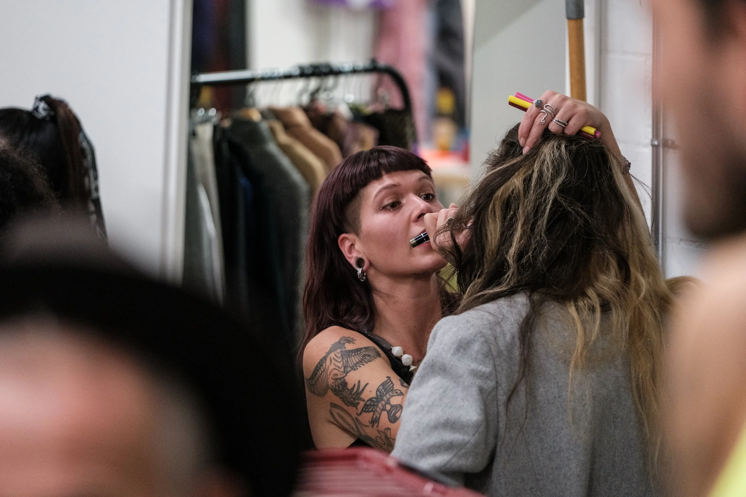 Eine Frau mit Tattoos im Arm lässt einem anderen Menschen Make-up im Backstage-Raum einer Modenschau machen.
