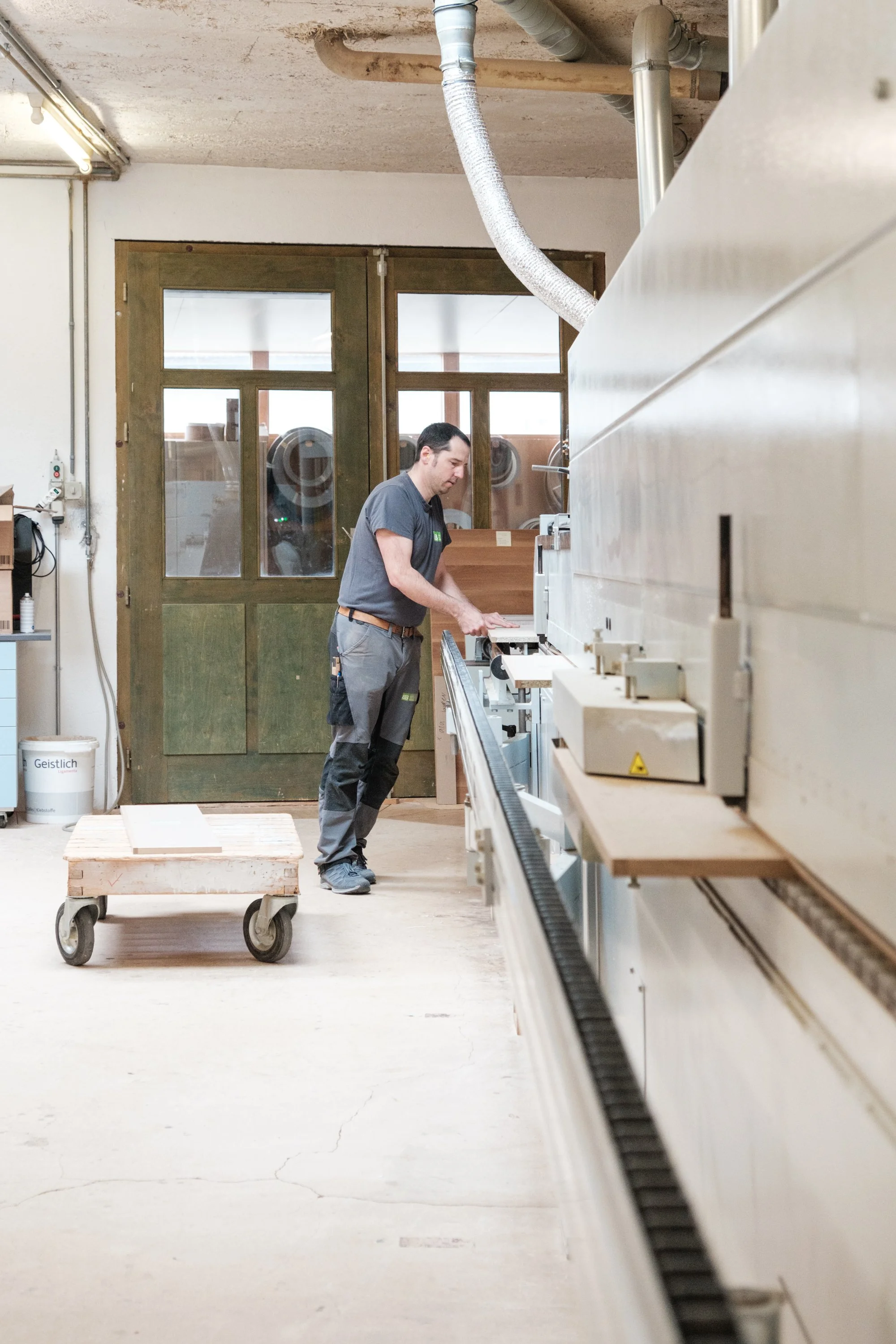 Mann arbeitet in einer Werkstatt an einer großen Maschine, vermutlich in der Fertigung oder im Holzbau.