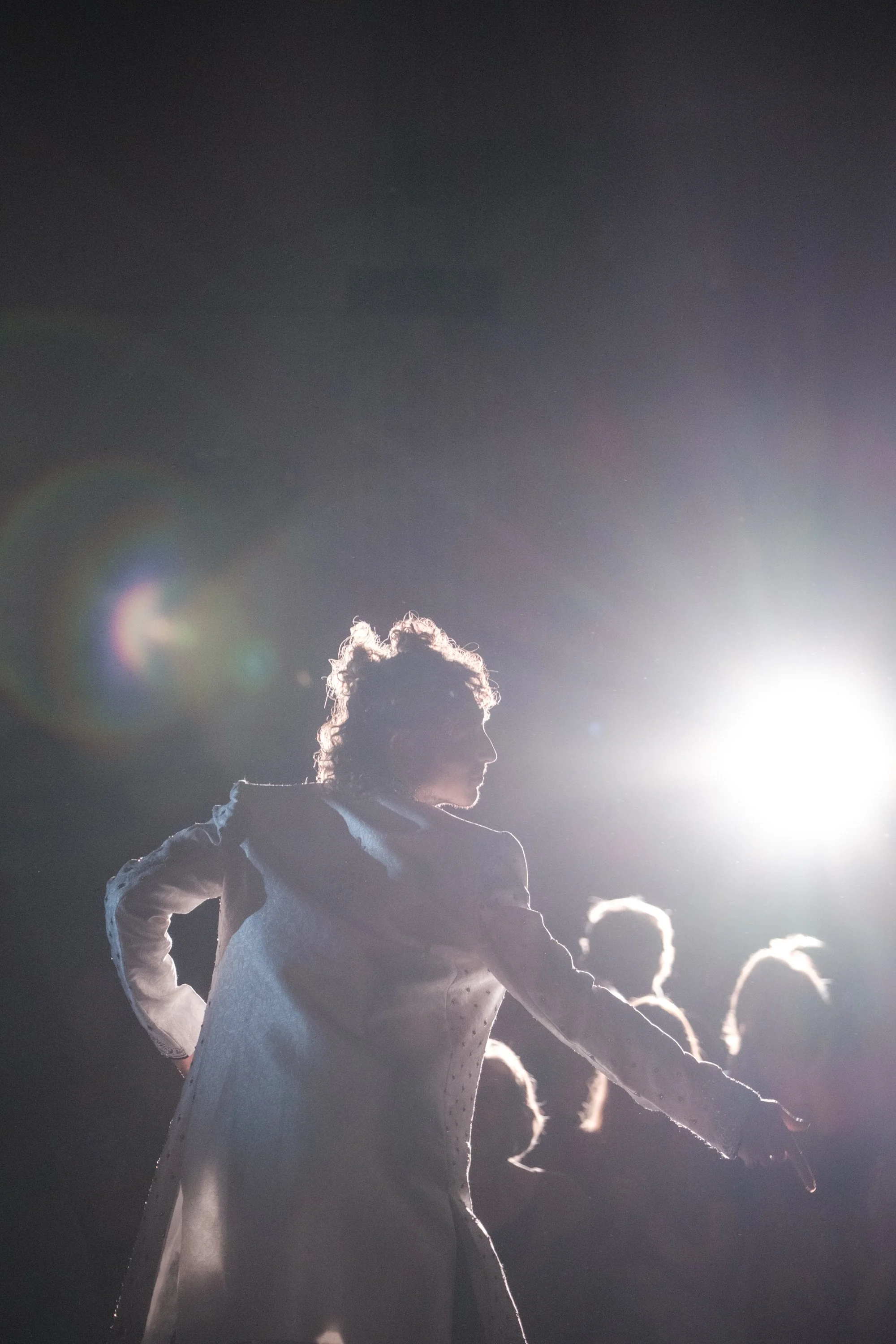 Schatten einer weiblichen Balletttänzerin beim Probieren eines weißen Kostüms vor einem hellen Lichtquell im Hintergrund.