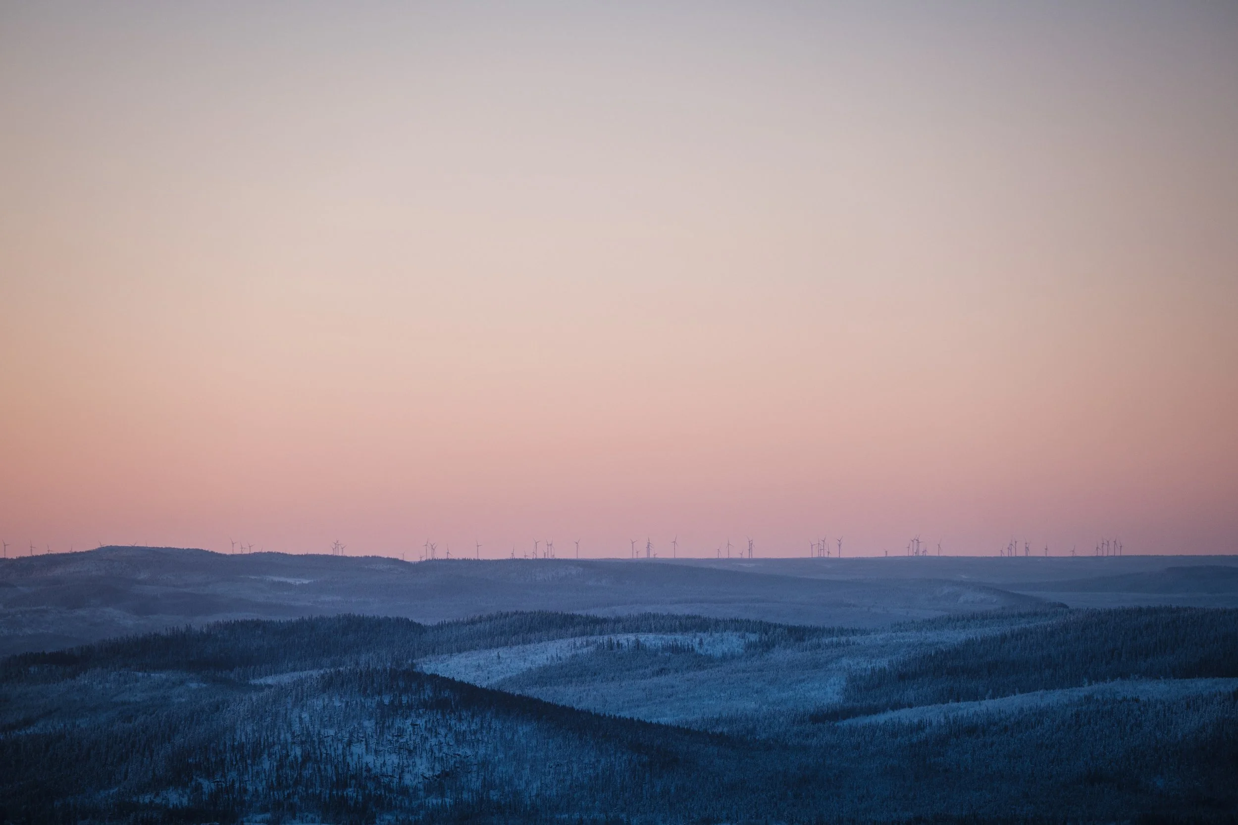 Berge mit schneebedeckten Gipfeln bei Sonnenuntergang, Windkraftanlagen im Hintergrund.