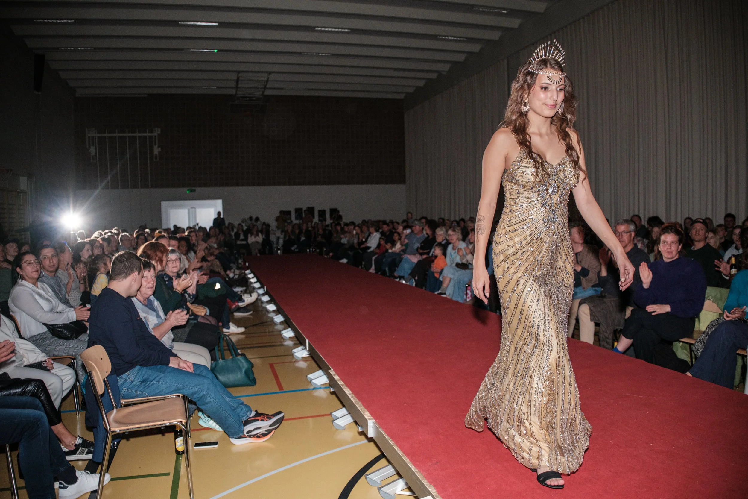 Model läuft auf der Bühne während einer Modenschau in einem großen Saal mit Publikum.